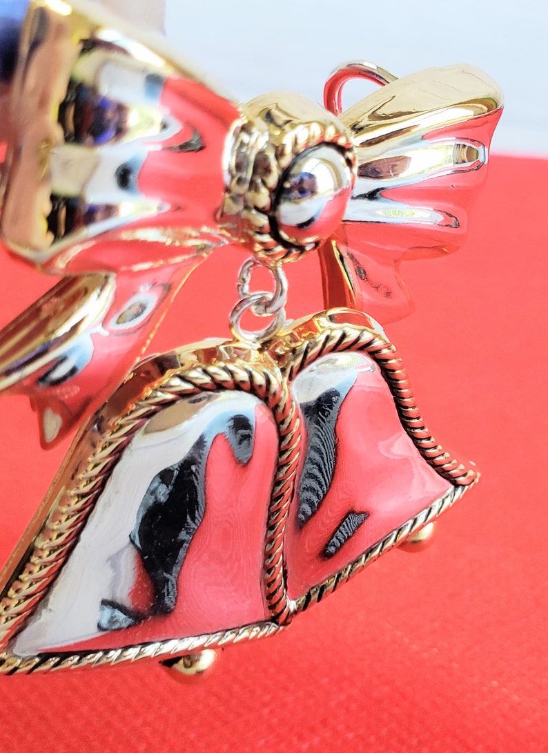 May include: A silver and gold Christmas ornament featuring two bells with a bow on top. The bells are decorated with a gold rope design.