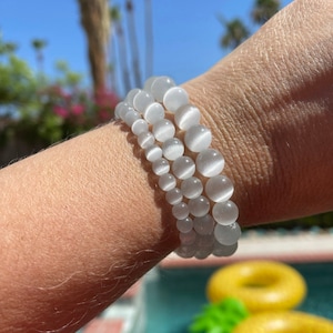 May include: Three white gemstone bracelets stacked on a person's wrist. The bracelets are made of round, smooth beads.