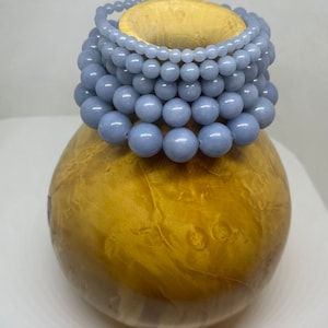 Puede incluir: Un conjunto de pulseras de piedras azules sobre un expositor de madera. Las pulseras est&aacute;n hechas de cuentas redondas y est&aacute;n dispuestas en tama&ntilde;o graduado.