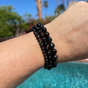 Op de afbeelding: Drie zwarte kralenarmbanden gestapeld op een pols. De armbanden zijn gemaakt van ronde, zwarte kralen met een licht glanzende afwerking.