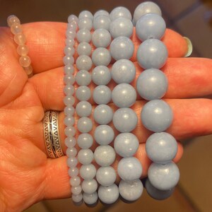 Puede incluir: Un conjunto de seis pulseras hechas con cuentas de piedras preciosas de color azul claro. Las pulseras est&aacute;n apiladas una encima de la otra y las est&aacute; sujetando una mano.