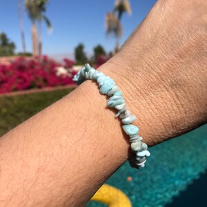 Könnte beinhalten: Ein hellblaues Edelstein-Armband aus kleinen, unregelmäßig geformten Steinen. Das Armband wird am Handgelenk getragen.