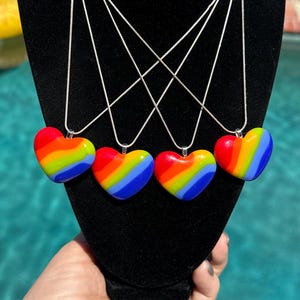 May include: Four silver chain necklaces with rainbow heart pendants. Each heart is made of colorful resin and features a swirl pattern of red, orange, yellow, green, blue, and purple.