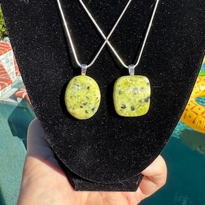 May include: Two silver chains with green and black stone pendants. The stones are oval and rectangular in shape.
