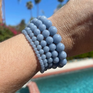 Puede incluir: Una pila de cinco pulseras de piedras preciosas azules con cuentas redondas. Las pulseras se llevan en la mu&ntilde;eca.