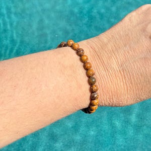 May include: A brown wooden beaded bracelet with intricate patterns on each bead. The bracelet is worn on a person's wrist.