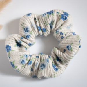 May include: A white ribbed scrunchie with a blue floral pattern. The scrunchie is made of a soft, stretchy fabric and is perfect for holding hair in place.