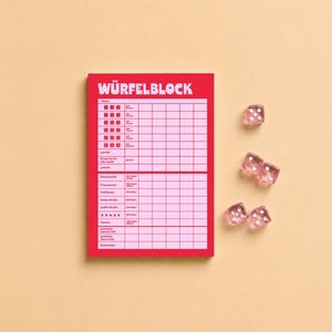 Könnte beinhalten: Ein roter und hellrosa Wertungsblock mit der Aufschrift WÜRFELBLOCK und einem Raster zur Erfassung von Spielergebnissen, begleitet von vier transparenten rosa Würfeln. Der Wertungszettel enthält Zeilen für verschiedene Kombinationen.