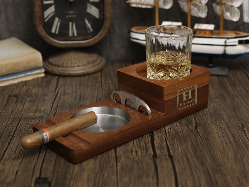 Puede incluir: Un soporte de madera para cigarros y whisky con un cortador de cigarros incorporado. El soporte tiene un compartimento para un vaso de whisky y un cenicero separado. El soporte est&aacute; personalizado con la letra "H" y el nombre "HARLAN".