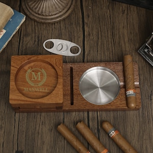 Puede incluir: Cenicero de madera para cigarros con un inserto de metal para ceniza, un cortador de cigarros incorporado y un compartimento separado para cigarros. El cenicero tiene una inscripci&oacute;n personalizada con la letra "M" y el nombre "MAXWELL".