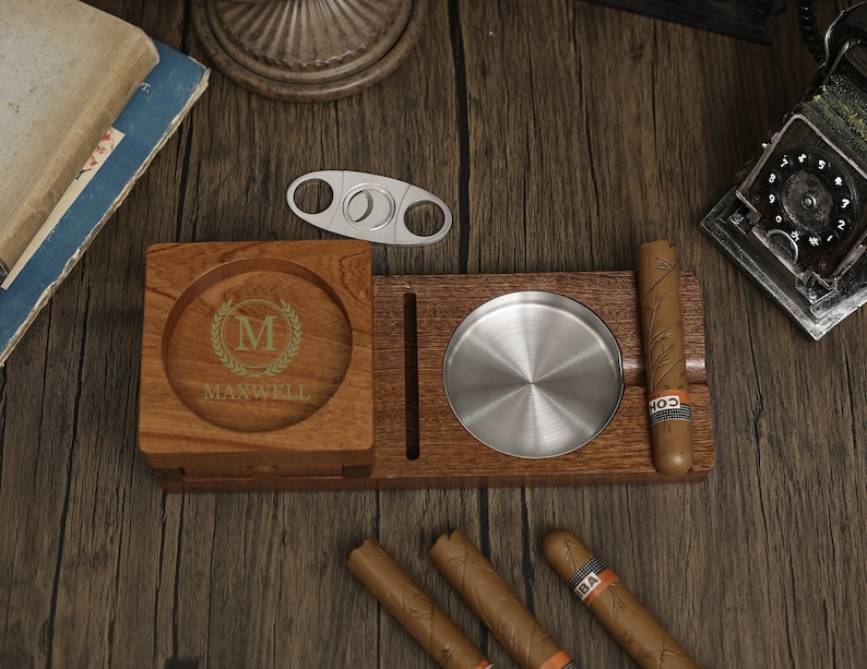 Puede incluir: Cenicero de madera para cigarros con un inserto de metal para ceniza, un cortador de cigarros incorporado y un compartimento separado para cigarros. El cenicero tiene una inscripci&oacute;n personalizada con la letra "M" y el nombre "MAXWELL".