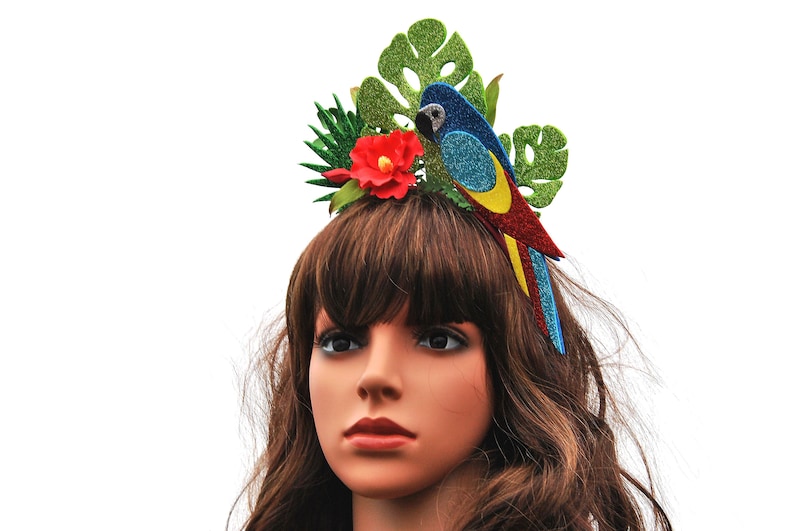 K&ouml;nnte beinhalten: Ein farbenfroher Papageien-Haarreifen mit gr&uuml;nen Bl&auml;ttern, einer roten Blume und blauen, gelben und roten Glitzerakzenten.