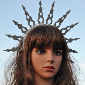 Puede incluir: Una corona de purpurina plateada con un dise&ntilde;o de estrella de explosi&oacute;n puntiaguda. La corona se lleva en un maniqu&iacute; con cabello casta&ntilde;o.