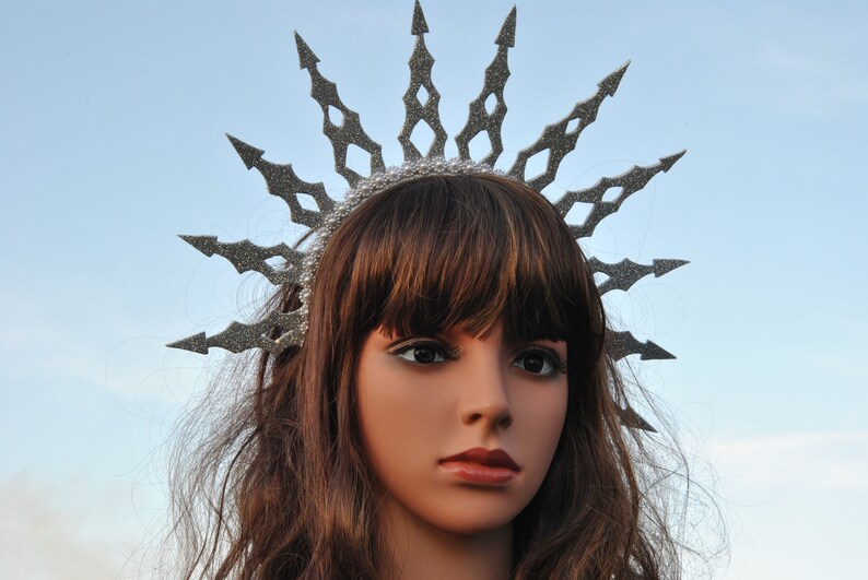 Puede incluir: Una corona de purpurina plateada con un dise&ntilde;o de estrella de explosi&oacute;n puntiaguda. La corona se lleva en un maniqu&iacute; con cabello casta&ntilde;o.