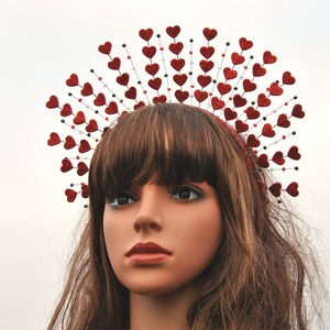 May include: A red glitter heart headband with a halo of smaller hearts. The headband is worn by a mannequin with long brown hair.