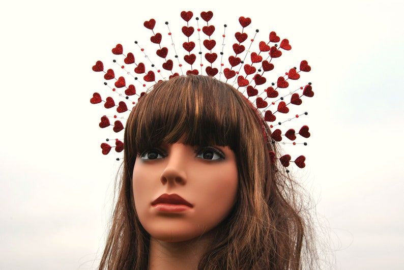 May include: A red glitter heart headband with a wire frame and black beads. The headband is worn by a mannequin with long brown hair.