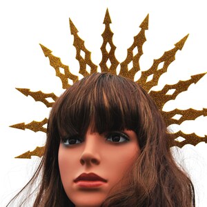 Puede incluir: Una corona de purpurina dorada con un dise&ntilde;o de estrella de explosi&oacute;n puntiaguda. La corona se lleva en un maniqu&iacute; con cabello casta&ntilde;o.