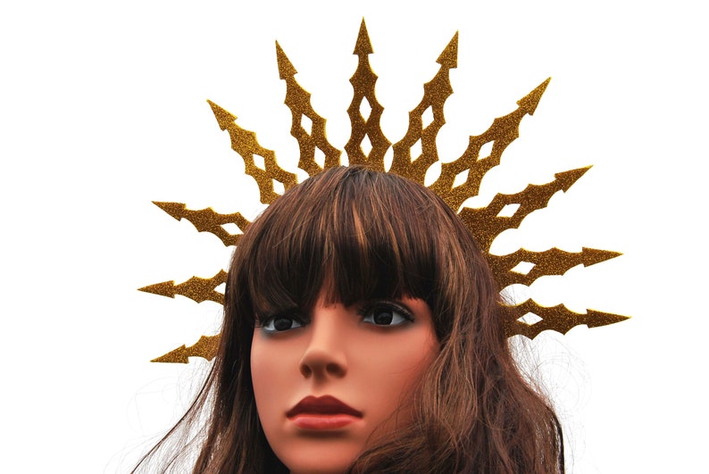Puede incluir: Una corona de purpurina dorada con un dise&ntilde;o de estrella de explosi&oacute;n puntiaguda. La corona se lleva en un maniqu&iacute; con cabello casta&ntilde;o.