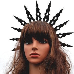 Puede incluir: Una mujer con una corona negra con puntas afiladas. La corona est&aacute; hecha de metal y tiene un dise&ntilde;o geom&eacute;trico. La mujer tiene el pelo largo y casta&ntilde;o y lleva una corona negra.