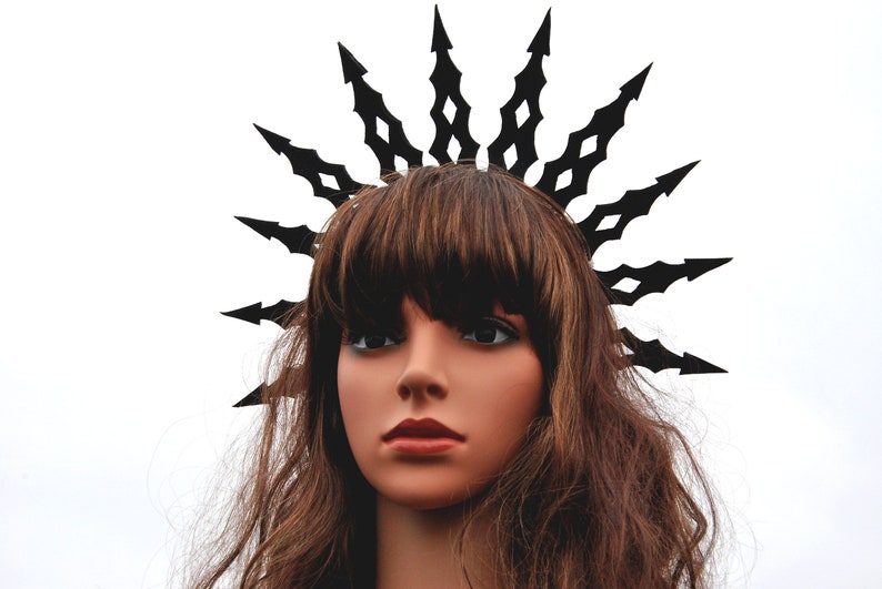 Puede incluir: Una mujer con una corona negra con puntas afiladas. La corona est&aacute; hecha de metal y tiene un dise&ntilde;o geom&eacute;trico. La mujer tiene el pelo largo y casta&ntilde;o y lleva una corona negra.