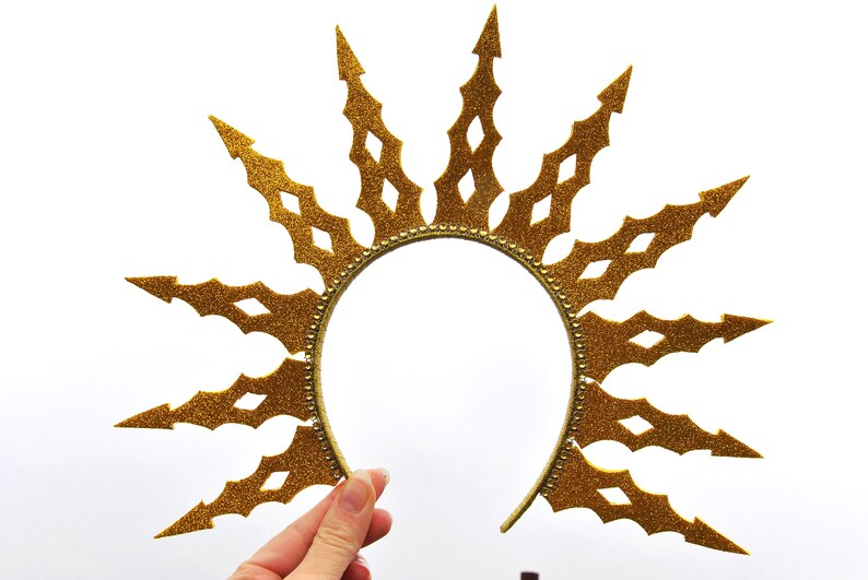 Puede incluir: Una diadema de purpurina dorada con un dise&ntilde;o de sol. La diadema est&aacute; hecha de un material flexible y tiene una forma puntiaguda en forma de estrella.