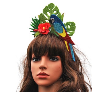 K&ouml;nnte beinhalten: Ein farbenfroher Papageien-Haarreifen mit gr&uuml;nen Bl&auml;ttern, einer roten Blume und blauen, gelben und roten Glitzerakzenten.