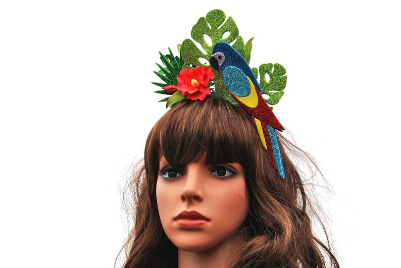 K&ouml;nnte beinhalten: Ein farbenfroher Papageien-Haarreifen mit gr&uuml;nen Bl&auml;ttern, einer roten Blume und blauen, gelben und roten Glitzerakzenten.
