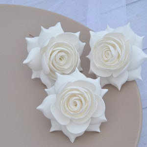 May include: Three white foam roses with a layered, ruffled design. The roses are arranged on a light brown plate.