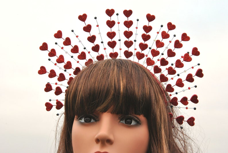 May include: A red glitter heart headband with a crown of hearts. The headband is made of wire and has a row of hearts around the top. The hearts are all red and have a glitter finish.
