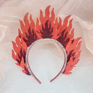 May include: A red and orange felt headband with a flame design. The headband is made of felt and has a silver wire frame.
