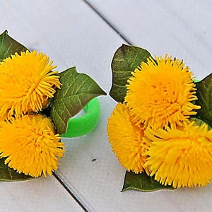 Puede incluir: Dos gomas para el pelo verdes decoradas con flores de diente de le&oacute;n amarillas y hojas verdes.