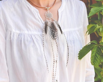 May include: A white shirt with a brown leather necklace featuring a silver dreamcatcher pendant with feathers.