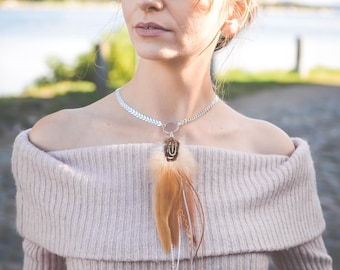 May include: A woman wearing a light pink off-the-shoulder sweater with a silver chain necklace with a brown feather pendant. The necklace has a small silver circle charm.