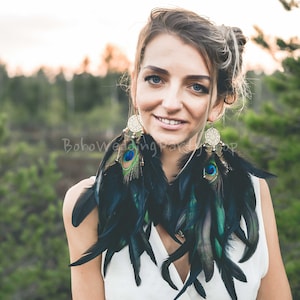 Könnte beinhalten: Auffällige Federohrringe in Schwarz und Türkis, mit goldfarbenen Metallakzenten und Pfauenfedern. Diese großen Ohrringe sind ein auffälliges Accessoire. Ein Statement-Schmuckstück im Boho-Stil.