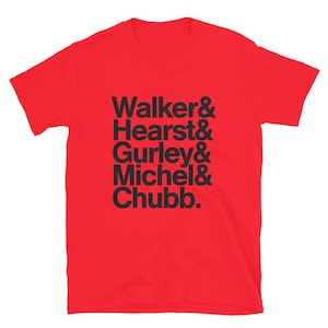 May include: Red short-sleeved t-shirt with black text that reads "Walker & Hearst & Gurley & Michel & Chubb."