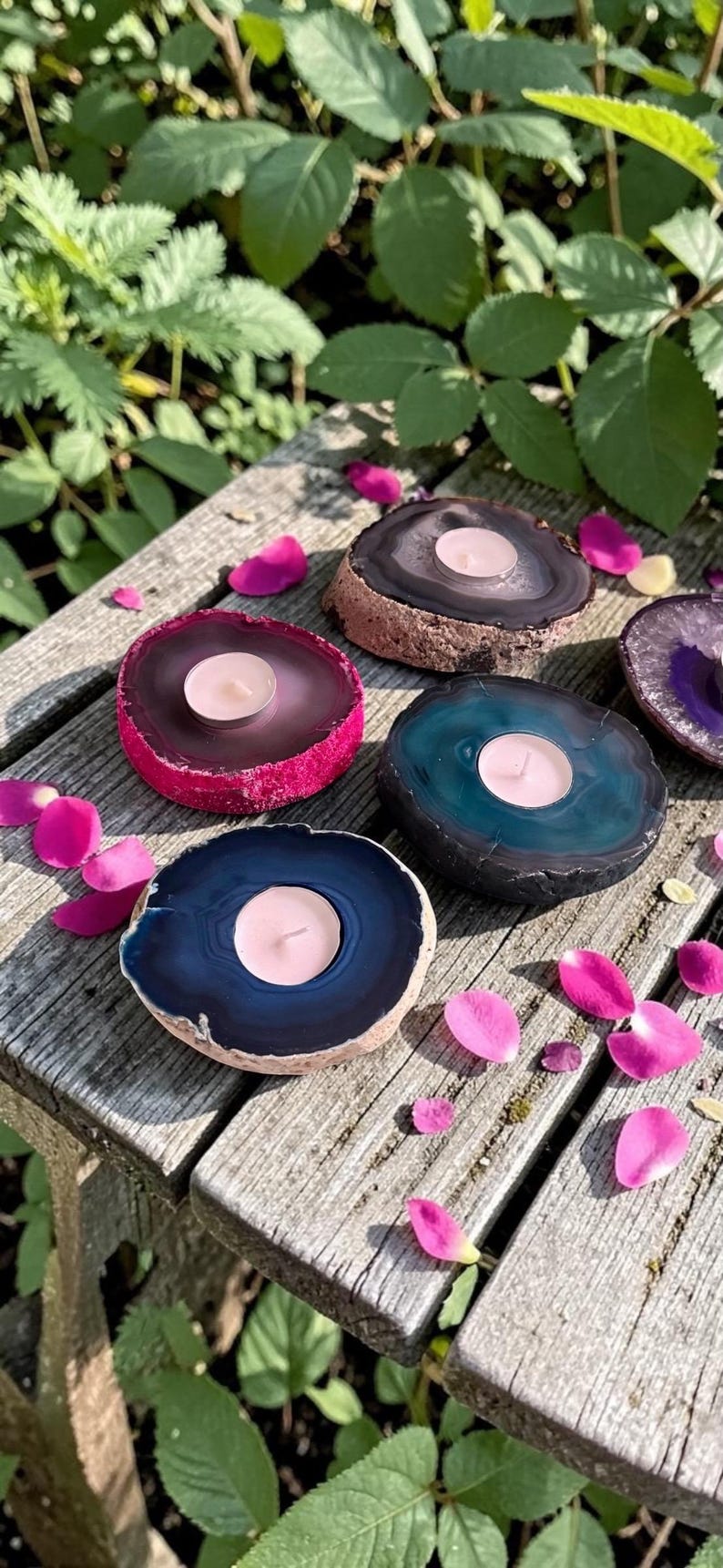May include: A collection of four circular agate stone candle holders, each featuring a polished, colorful center and a natural, rough-textured outer edge. Each stone holds a small, round, white tea light candle in its center, displaying shades of pink, teal, and dark blue.
