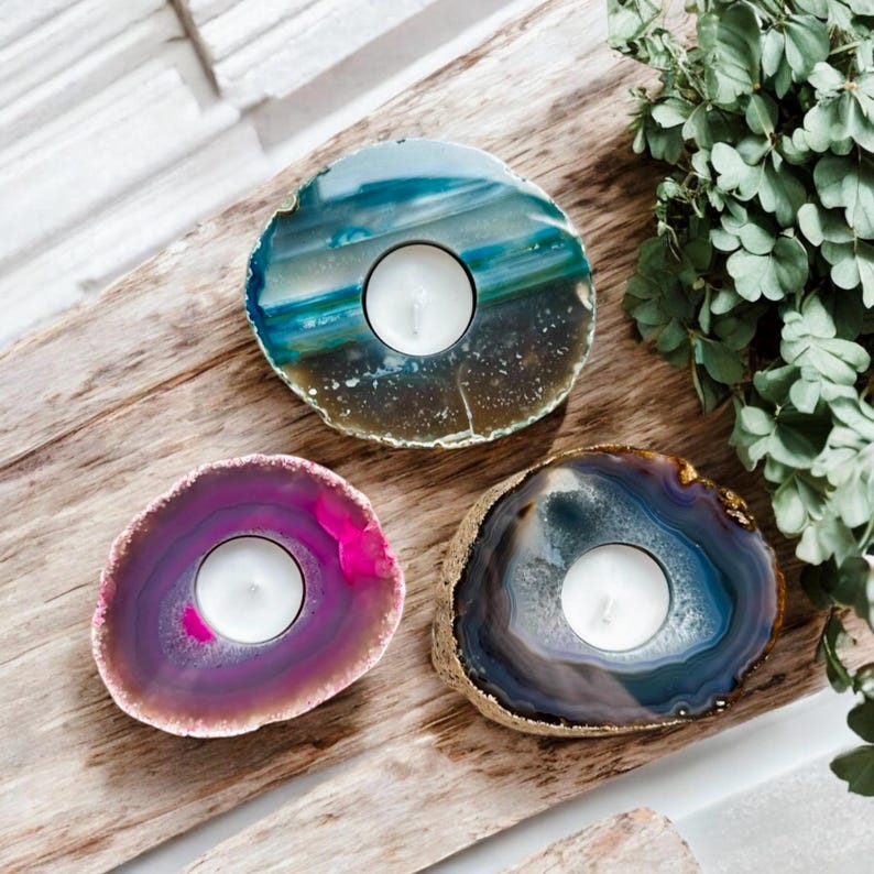 May include: Three circular tea light candle holders crafted from polished agate slices. One holder features teal and blue banding, another displays vibrant pink and magenta hues, and the third shows deep blue and grey tones with gold-toned edges.