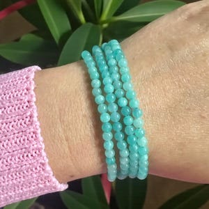 May include: A multi-strand bracelet composed of small, round, polished turquoise-coloured beads. The beads are uniform in size and strung together to create a layered appearance, wrapping around the wrist in a continuous, circular formation.