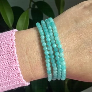 May include: A multi-strand bracelet composed of small, smooth, round turquoise-coloured gemstone beads. The bracelet wraps around the wrist in four distinct rows, featuring a consistent light blue-green hue and a polished, uniform bead texture.