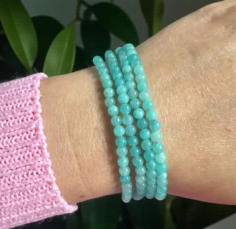 May include: A multi-strand bracelet composed of small, smooth, round turquoise-coloured gemstone beads. The bracelet wraps around the wrist in four distinct rows, featuring a consistent light blue-green hue and a polished, uniform bead texture.