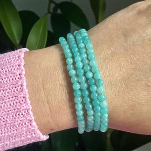 May include: A multi-strand bracelet composed of small, smooth, round turquoise-coloured gemstone beads. The bracelet wraps around the wrist in four distinct rows, featuring a consistent light blue-green hue and a polished, uniform bead texture.