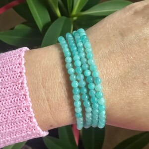 May include: A multi-strand bracelet composed of small, round, polished turquoise-coloured beads. The beads are uniform in size and strung together to create a layered appearance, wrapping around the wrist in a continuous, circular formation.