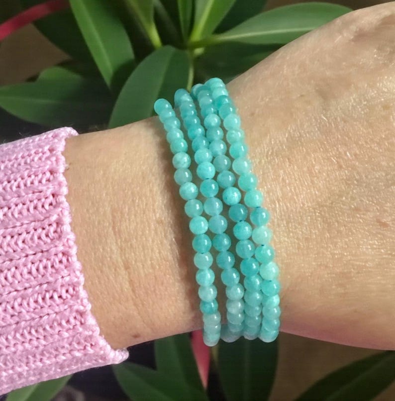 May include: A multi-strand bracelet composed of small, round, polished turquoise-coloured beads. The beads are uniform in size and strung together to create a layered appearance, wrapping around the wrist in a continuous, circular formation.