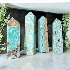 May include: Four polished stone obelisks in varying shades of blue and brown. The obelisks are rectangular with pointed tops. The stones have a marbled appearance, with streaks of color throughout. The obelisks are arranged in a row.