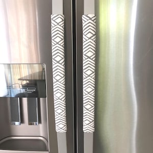 May include: Refrigerator handle covers with a geometric diamond pattern in gray and white. The covers are wrapped around the stainless steel handles of a refrigerator.