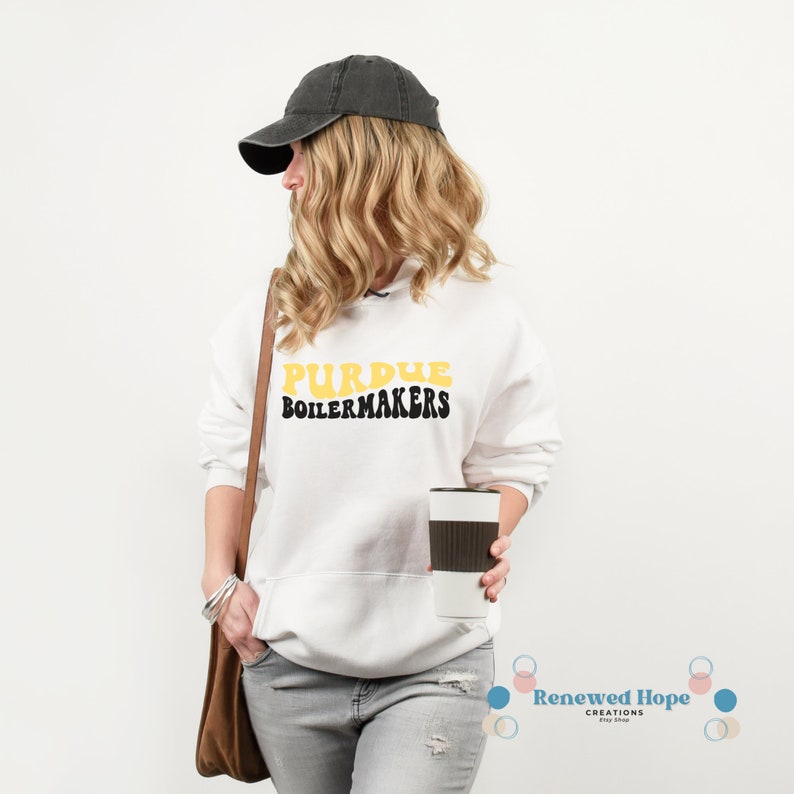 Caucasian female with gray hat, purse, and coffee cup wearing a stylish Purdue Boilermaker white hooded sweatshirt, showcasing the SVG design available for instant download.
