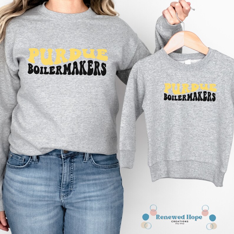 Caucasian female wearing a stylish Purdue Boilermaker gray sweatshirt,  and holding a child size gray sweatshirt on a hanger- showcasing the SVG design available for instant download.