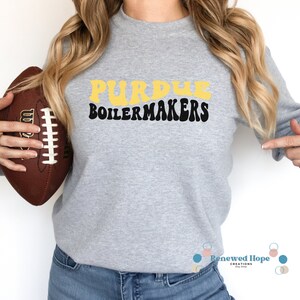 Caucasian female with football in hand wearing a stylish Purdue Boilermaker gray crewneck sweatshirt showcasing the SVG design available for instant download.
