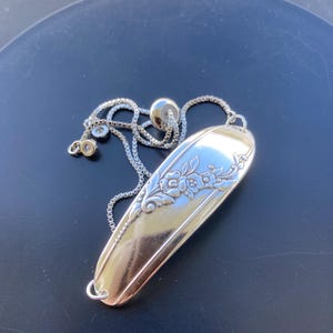 May include: A silver bracelet with a floral design on a spoon-shaped charm. The bracelet is adjustable with a chain and a bead.