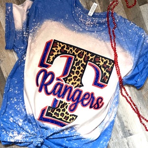 May include: A blue and white bleached t-shirt with a leopard print "T" and the word "Rangers" in blue glitter.